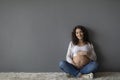 Beautiful Happy Pregnant Woman Sitting On Floor And Tenderly Embracing Belly