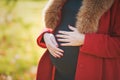 Beautiful happy pregnant woman staying in autumn park touching her belly and enjoying expecting of baby. Royalty Free Stock Photo