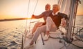 Beautiful and happy senior couple in love sitting on the side of sailboat or yacht deck floating in sea at sunset and Royalty Free Stock Photo