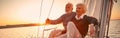 Beautiful and happy senior couple in love sitting on the side of sailboat or yacht deck floating in sea at sunset and Royalty Free Stock Photo