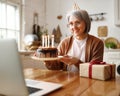 Beautiful happy senior woman with cake with lit candles , celebrating birthday online with family Royalty Free Stock Photo