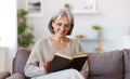 Beautiful happy senior woman with grey hair in eyeglasses reading book and smiling Royalty Free Stock Photo