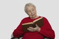 Beautiful happy senior woman with grey hair reading book and smiling while resting at home Royalty Free Stock Photo