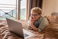 Beautiful happy smiling gray-haired mature woman in glasses lying on bed at home in front of laptop screen. Pensioner using modern Royalty Free Stock Photo