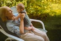 Beautiful happy smiling senior elderly woman holding on hands cute little baby boy sitting outdoor. Grandmother grandson