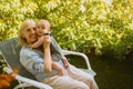 Beautiful happy smiling senior elderly woman holding on hands cute little baby boy sitting outdoor. Grandmother grandson Royalty Free Stock Photo