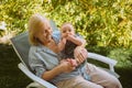 Beautiful happy smiling senior elderly woman holding on hands cute little baby boy sitting outdoor. Grandmother grandson