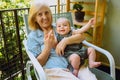 Beautiful happy smiling senior elderly woman holding on hands cute little baby boy sitting on outdoor rocking chair Royalty Free Stock Photo