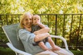 Beautiful happy smiling senior elderly woman holding on hands cute little baby boy sitting on outdoor rocking chair Royalty Free Stock Photo