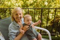 Beautiful happy smiling senior elderly woman holding on hands cute little baby boy sitting on outdoor rocking chair Royalty Free Stock Photo