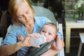 Beautiful happy smiling senior elderly woman nanny feeding formula on hands from bottle cute little baby boy Royalty Free Stock Photo