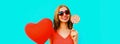 Beautiful happy smiling young woman with lollipop and bunch of red heart shaped balloons wearing sunglasses on blue background Royalty Free Stock Photo