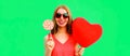 Beautiful happy smiling young woman with lollipop and bunch of red heart shaped balloons wearing sunglasses on green background Royalty Free Stock Photo