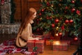 Beautiful happy smiling young woman putting Christmas gift under the xmas tree at cozy living room.