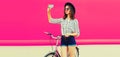 Beautiful happy smiling young woman taking selfie by smartphone with bicycle wearing shirt, shorts, black round hat on pink Royalty Free Stock Photo