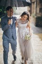 Beautiful happy wedding couple embracing together under umbrella in sunny rainy street. Stylish bride and groom walking and Royalty Free Stock Photo