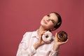 Beautiful happy woman holding donuts, looking up, smiling and posing against red background. Concept of delicious pastries, Royalty Free Stock Photo