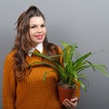 Beautiful happy woman holding plant in vase against gray background Royalty Free Stock Photo