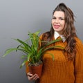 Beautiful happy woman holding plant in vase against gray background Royalty Free Stock Photo