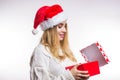 Beautiful happy woman in red Santa hat and beige sweater opens her Christmas gift, box with ribbon. New year, birthday and Royalty Free Stock Photo