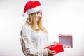 Beautiful happy woman in red Santa hat and beige sweater opens her Christmas gift, box with ribbon Royalty Free Stock Photo