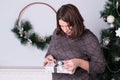 Beautiful happy woman sits next to a Christmas tree with a gift in her hands, a woman opens a New Year`s gift Royalty Free Stock Photo