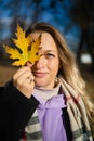 Middle aged woman with a smile holds an autumn yellow leaf near the face
