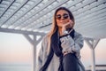 Beautiful happy woman in sunglasses standing at the sea, girl in grey coat