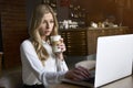 Beautiful happy woman working on laptop computer during coffee break in cafe bar. Young blonde girl in white blouse Royalty Free Stock Photo