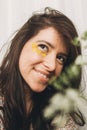 Beautiful happy woman with yellow petals on face posing with wildflowers in sunny room. Portrait of young brunette in boho dress Royalty Free Stock Photo