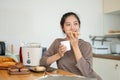 A beautiful and happy young Asian woman is enjoying her toast and coffee in the kitchen Royalty Free Stock Photo