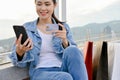 Woman using her phone, holding a credit card, sitting on the city mall`s rooftop with shopping bags Royalty Free Stock Photo