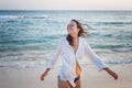 Beautiful happy young brunette woman in a white shirt enjoys enjoying life near the ocean at sunset