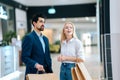 Beautiful happy young couple holding shopping paper bags with purchases and looking upon showcase at mall. Royalty Free Stock Photo