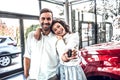 Beautiful happy young couple hugging holding the keys to their new car smiling joyfully at the dealership Royalty Free Stock Photo