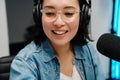 Happy young female radio host using microphone and headphones while broadcasting in studio Royalty Free Stock Photo