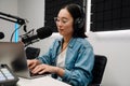 Beautiful young female radio host using microphone and laptop while broadcasting in studio Royalty Free Stock Photo