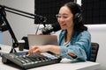 Happy young female radio host using microphone and sound mixer while broadcasting in studio Royalty Free Stock Photo