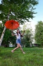 beautiful happy young girl with an orange umbrella is having fun on sunny summer day outdoors against the background of green Royalty Free Stock Photo