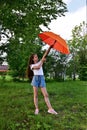 beautiful happy young girl with an orange umbrella on sunny summer day outdoors against a background of green foliage, dressed in Royalty Free Stock Photo
