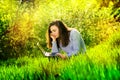 Beautiful happy young girl sits in a park on a glade with a laptop in green grass. sunny day Royalty Free Stock Photo