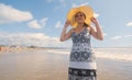 Beautiful happy young Hispanic woman walking alone on the beach wearing a hat and black and white dress during a sunny morning Royalty Free Stock Photo