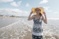 Beautiful happy young Hispanic woman walking alone on the beach wearing a hat and black and white dress during a sunny morning Royalty Free Stock Photo