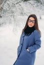 Beautiful happy young woman with black glasses wearing winter coat color Blue Cobalt and black scarf covered with snow Royalty Free Stock Photo