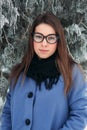 Beautiful happy young woman with black glasses wearing winter coat color Blue Cobalt and black scarf covered with snow Royalty Free Stock Photo