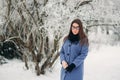 Beautiful happy young woman with black glasses wearing winter coat color Blue Cobalt and black scarf covered with snow Royalty Free Stock Photo