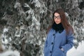 Beautiful happy young woman with black glasses wearing winter coat color Blue Cobalt and black scarf covered with snow Royalty Free Stock Photo