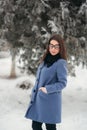 Beautiful happy young woman with black glasses wearing winter coat color Blue Cobalt and black scarf covered with snow Royalty Free Stock Photo