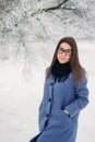 Beautiful happy young woman with black glasses wearing winter coat color Blue Cobalt and black scarf covered with snow Royalty Free Stock Photo