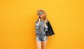 Beautiful happy young woman calling on phone with shopping bag looking away wearing summer straw hat, denim jacket on yellow Royalty Free Stock Photo